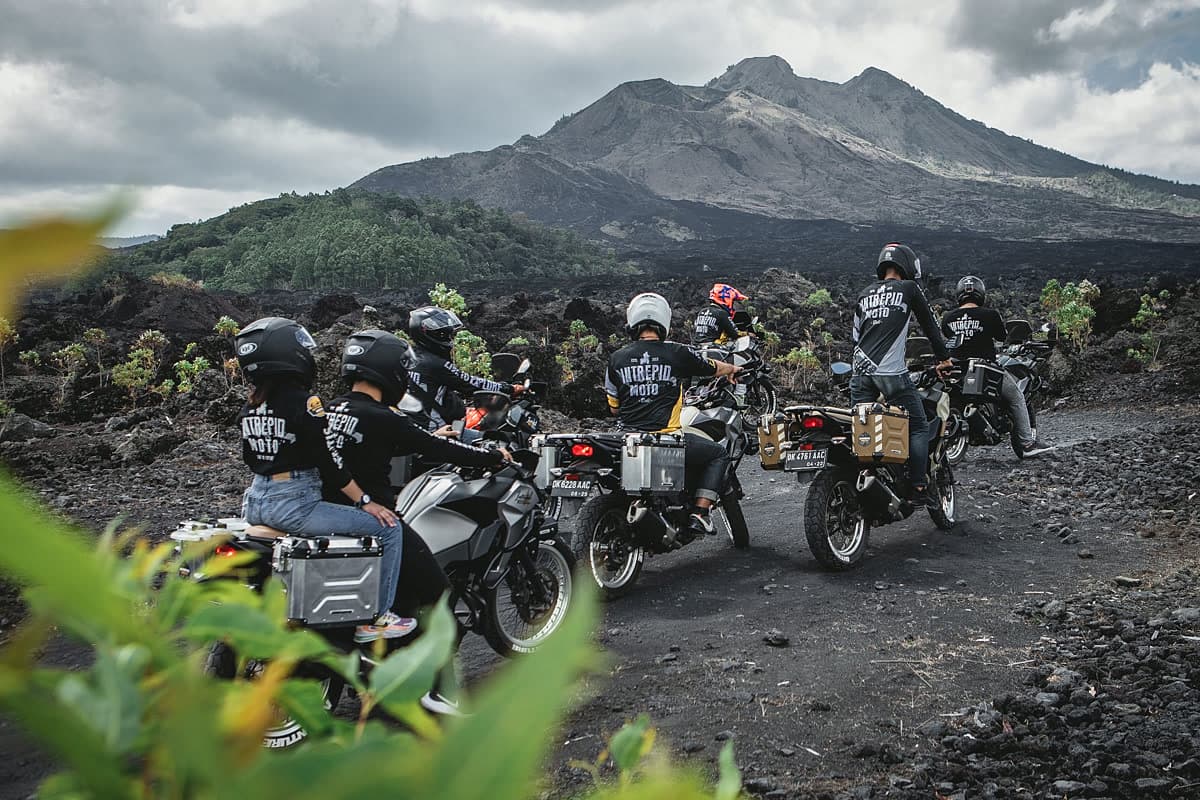 A group of motorcycle riders facing a volcano across a lava field